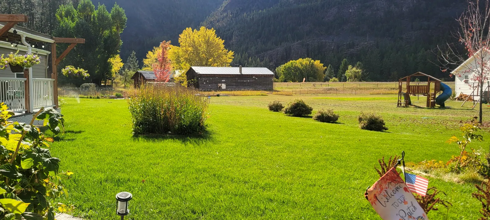 A thick green lawn in fall with garden beds, shrubs and a valley behind it